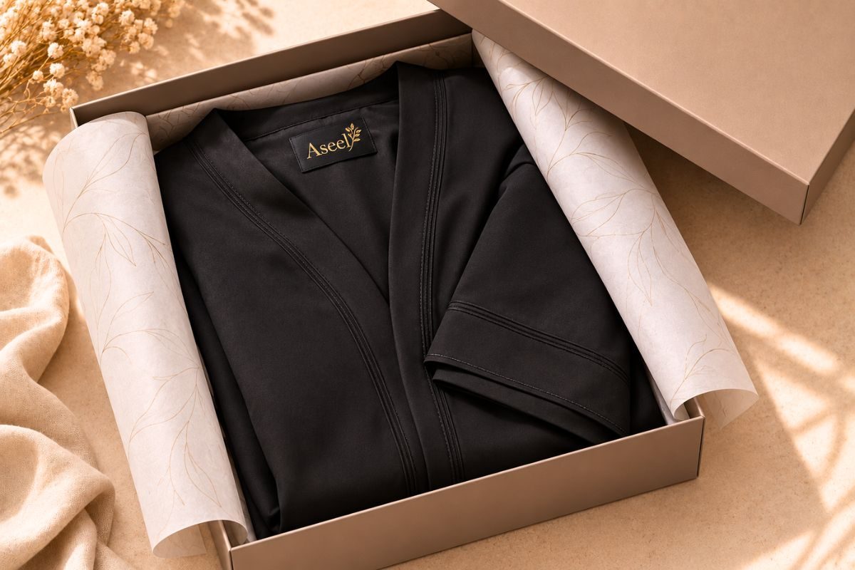 Folded abaya inside an open taupe box with tissue lining